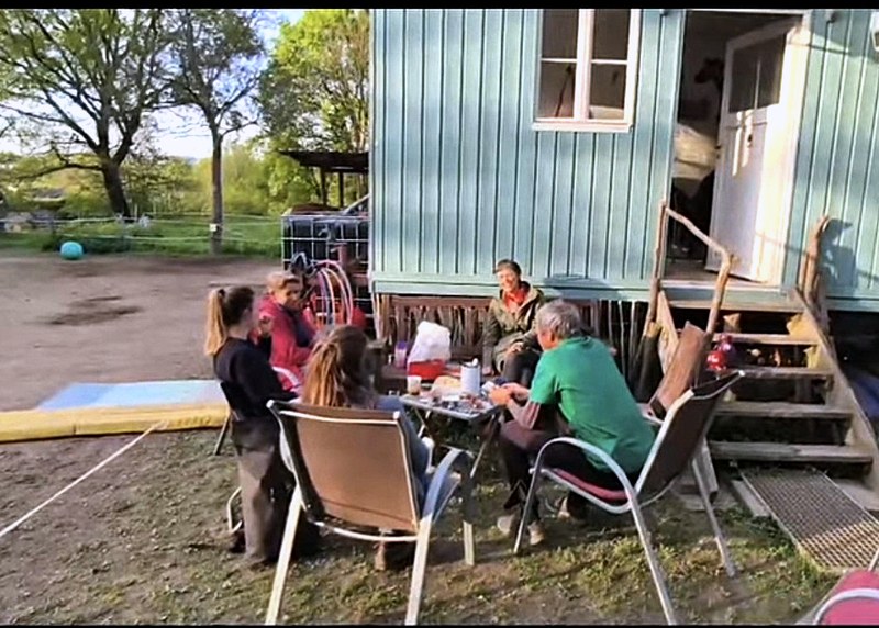 Eine Gruppe sitzt vor dem Bauwagen am Tisch